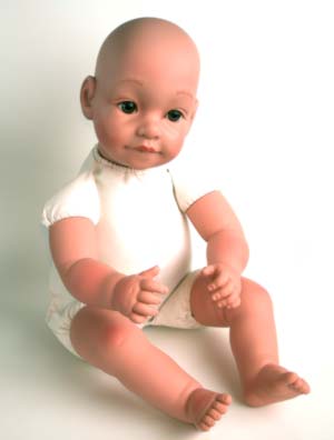 A baby doll sitting on the floor wearing white clothes.