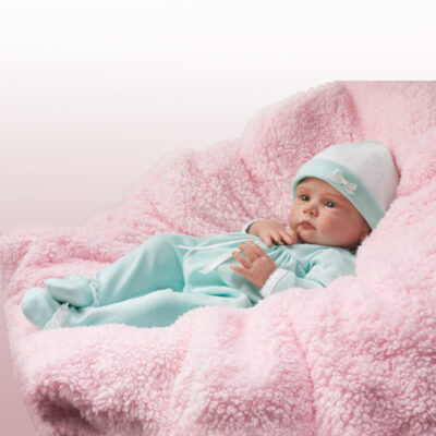 A baby in blue pajamas laying on pink blanket.
