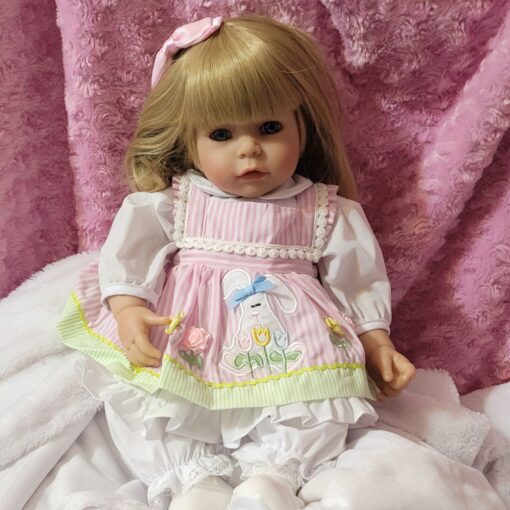 A doll sitting on top of a bed next to a pink curtain.