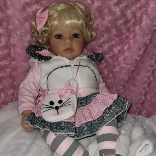 A doll is sitting on the bed wearing pajamas.