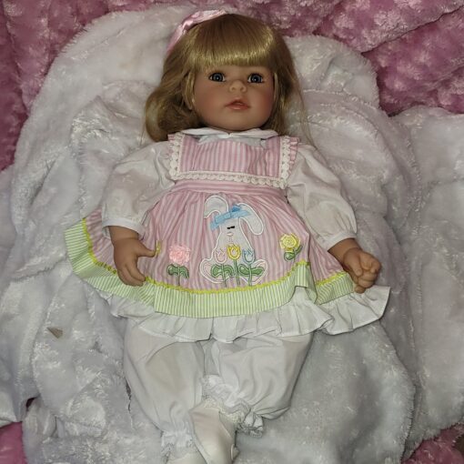 A doll is laying on the bed with her head down.